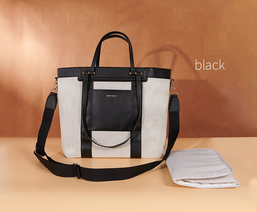 Multi-pocket black diaper tote bag on shoulder of a mom