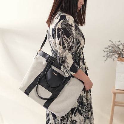 Mom holding canvas diaper handbag at a park with stroller nearby